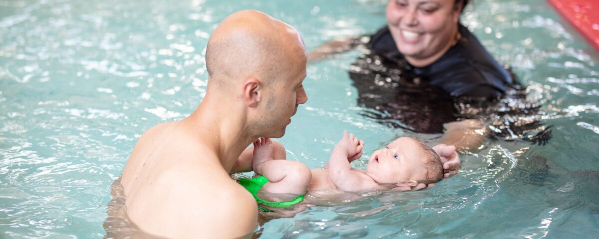 Two swimming trainers help a toddler to swim in San Francisco, CA