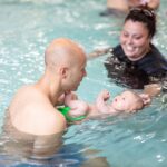 Two swimming trainers help a toddler to swim in San Francisco, CA