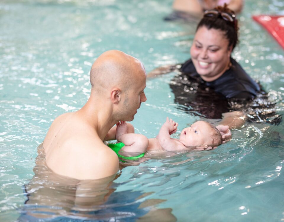 Two swimming trainers help a toddler to swim in San Francisco, CA