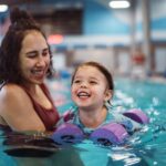 A woman trainer helps a toddler swim during lessons in San Francisco, CA, building water confidence.