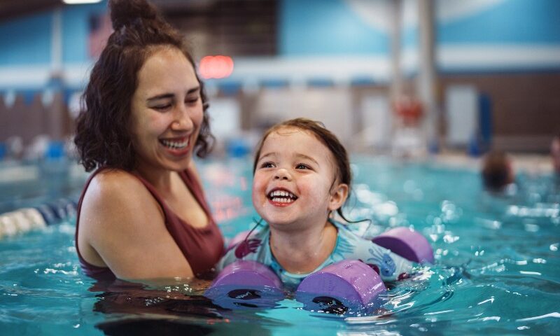 A woman trainer helps a toddler swim during lessons in San Francisco, CA, building water confidence.