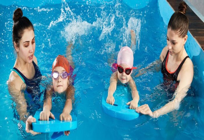 Two women & two kids in goggles splash in a pool, showing swim do’s and don’ts in San Francisco, CA.