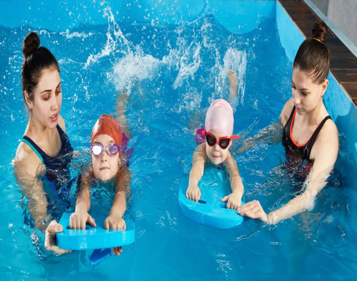Two women & two kids in goggles splash in a pool, showing swim do’s and don’ts in San Francisco, CA.